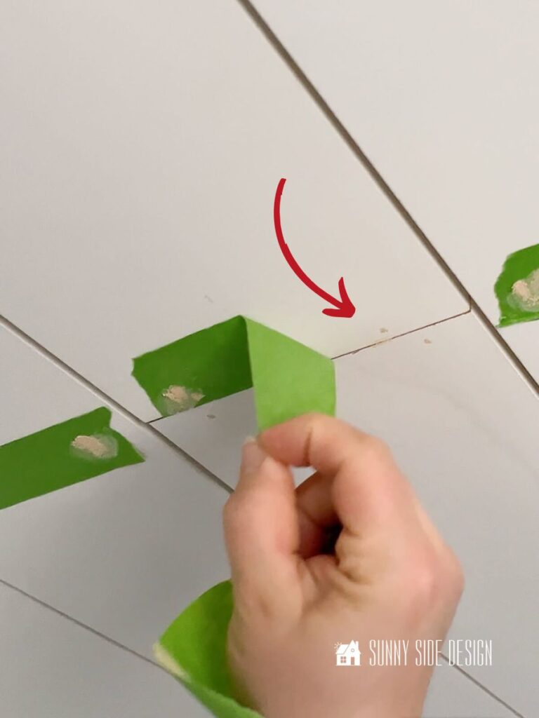 Pulling back painters tape to reveal small circle of dried wood filler on shiplap bathroom ceiling.