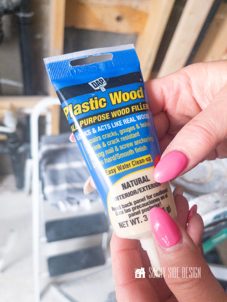 Woman holds wood filler, used to fill in nail holes in the shiplap ceiling.