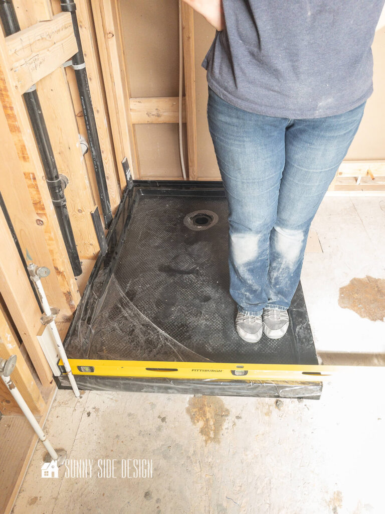 Install a prefab shower pan over the wet mortar, a level is placed on end of shower pan to check level.