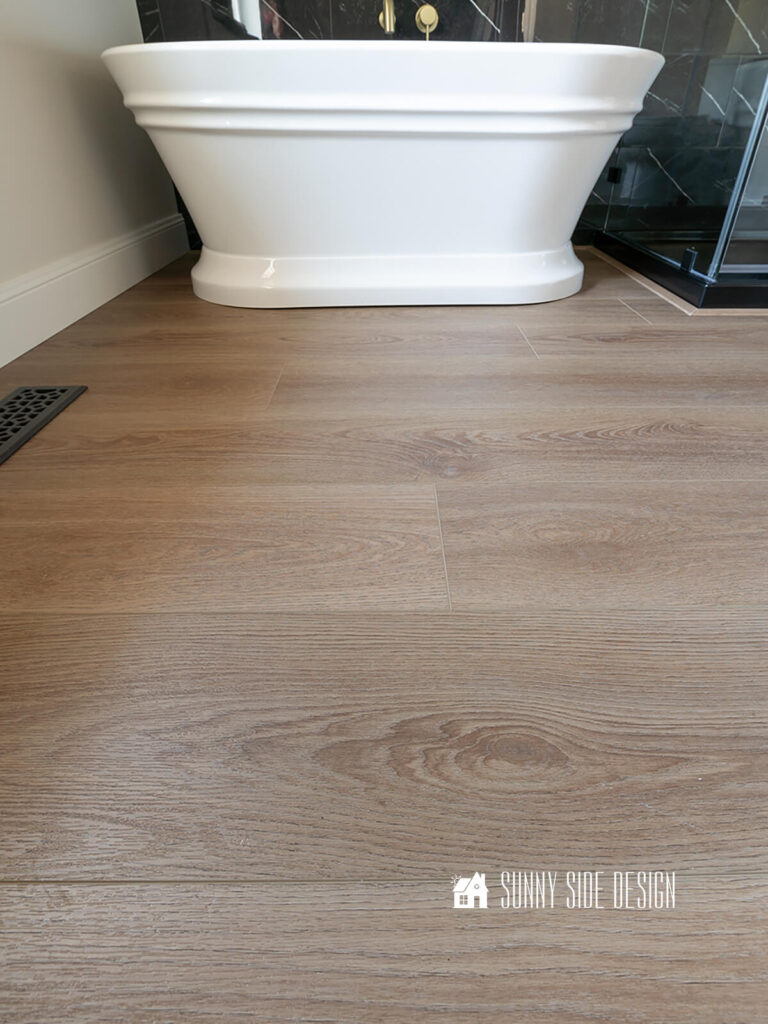 Completed vinyl plank flooring in a bathroom with a freestanding tub, black marble tile and a glass shower enclosure.