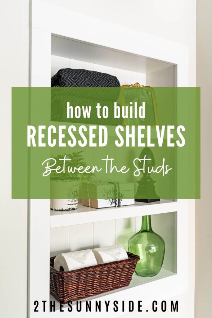 Pinterest Image: How to Build Simple a Recessed Shelf in a Wall Between the Studs. Decorated bathroom wall niche with green glass vase, basket with toilet paper, black towels, potted plant, gold framed photograph, finial, and book stack.