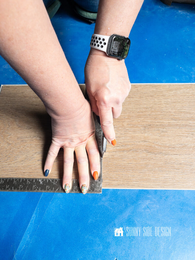 Woman using a framing square scores the vinyl plank for the next cut.