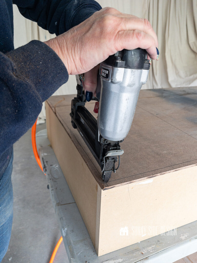 Woman attaches shiplap backing to shelves with an 18 guage brad nailer.