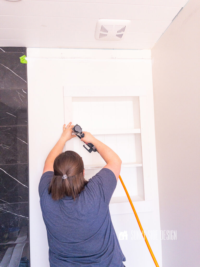 Woman attached trim to recessed sheves with a brad nail gun.