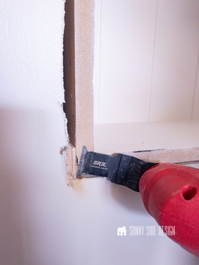 An oscillating tool is used to cut off the excess wood shims when installing the recessed shelves in a bathroom wall.