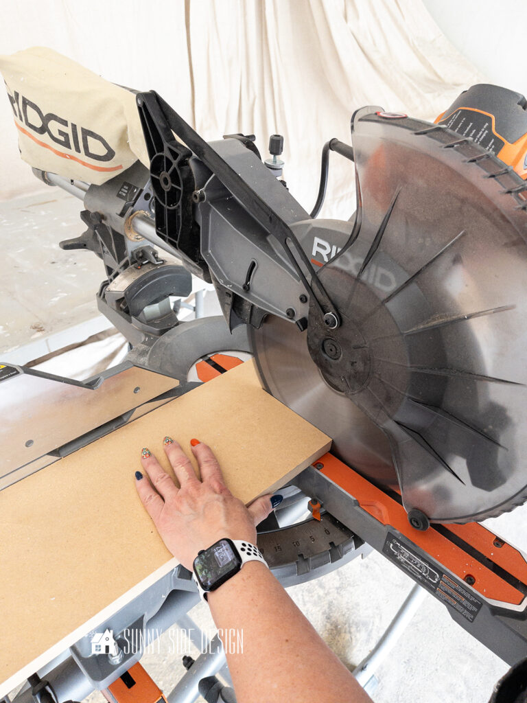 Woman's hands on a mitre saw cutting down wood for the recessed shelf in a wall.