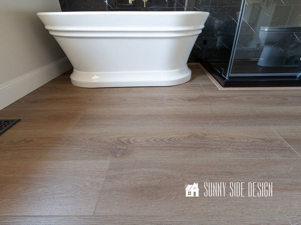 Completed vinyl plank flooring in a bathroom with a freestanding tub, black marble tile and a glass shower enclosure.