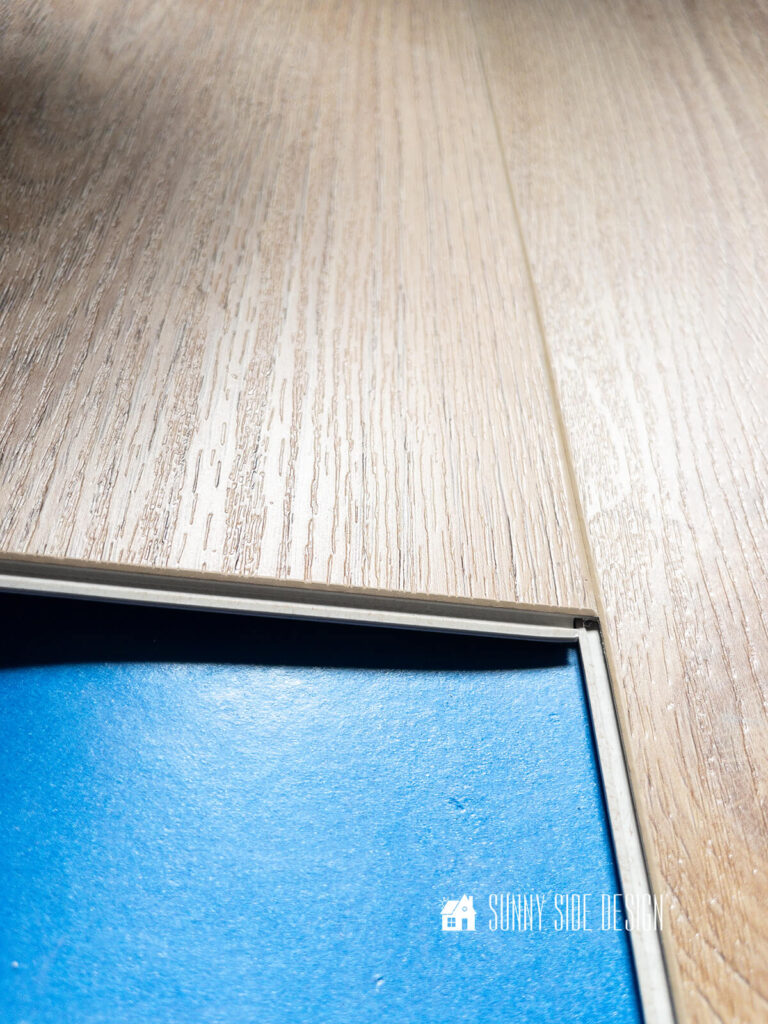 Vinyl plank flooring is attached to previous row, tilting at a 45° angle and snapping into place.