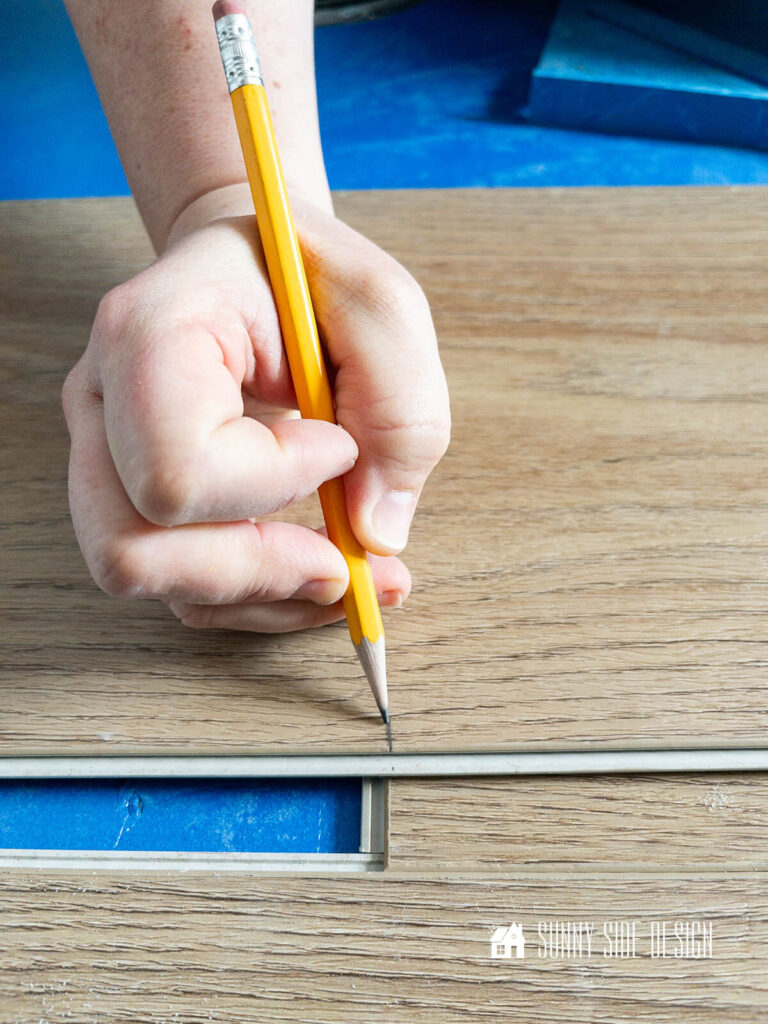Woman marked with a pencil for the next cut when installing a luxury vinyl plank floor.