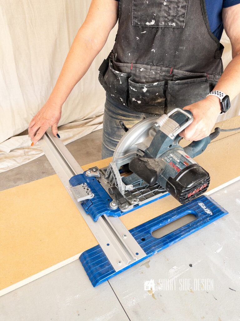 Woman holding a circular saw with a ripcut guide to cut down all of the wood to 7" wide for the recessed shelf in a wall.
