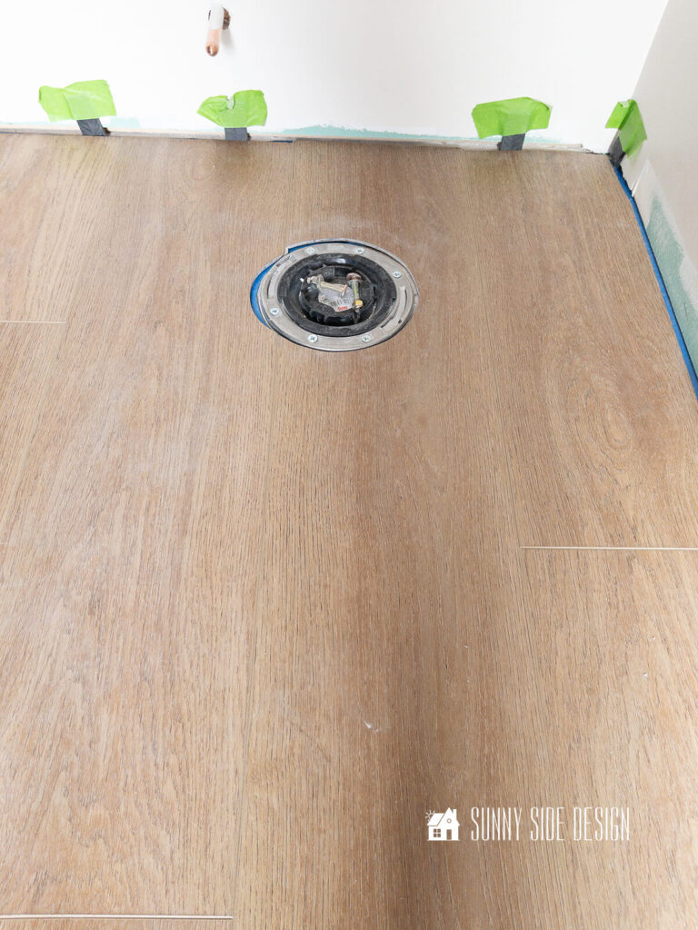 Luxury vinyl plank is cut out around sewer pipe for toilet.