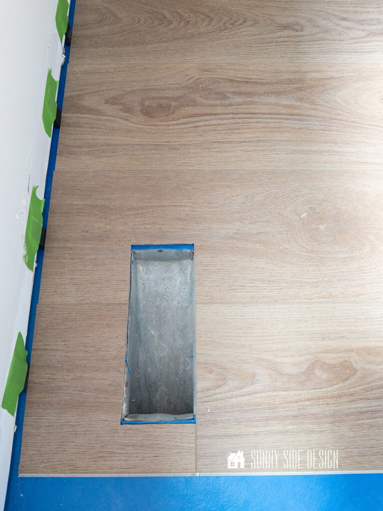 Luxury vinyl plank flooring is cut our to fit openings for heat vents.
