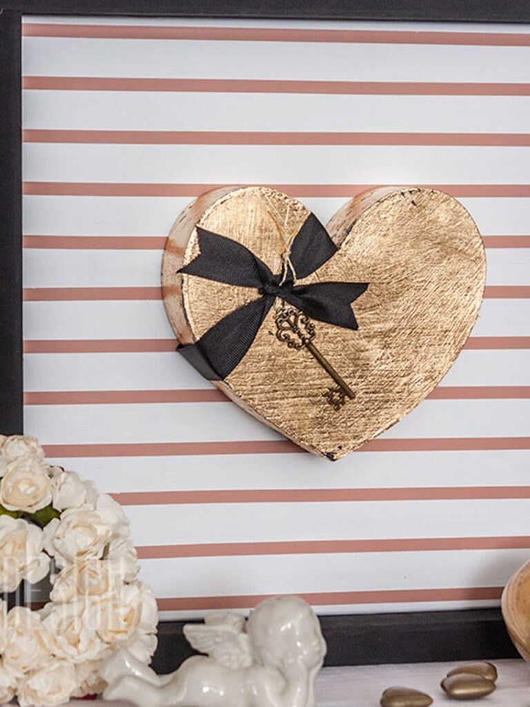 Easy Valentine's Day decor with a gold leaf heart mounted on a blush and white pin stripped frame with other various hearts and white cherubs.