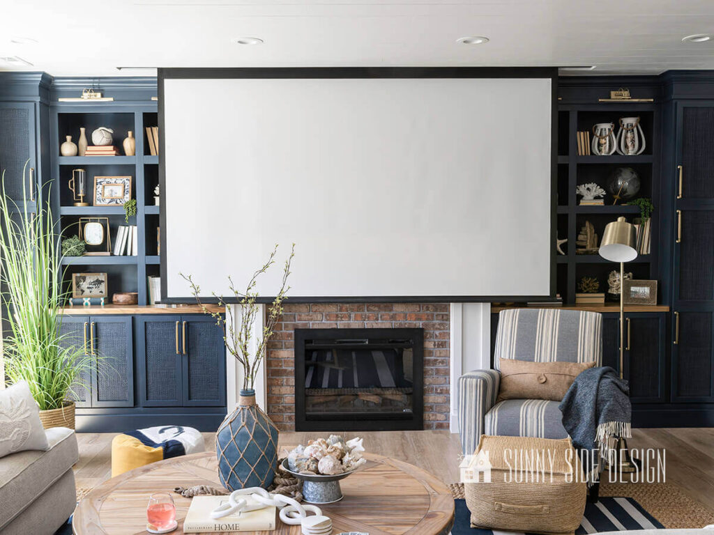 Movie screen lowered down in front of the fireplace and built ins. Blue and white striped chair with brass floor lamp, round plank wood coffee table.