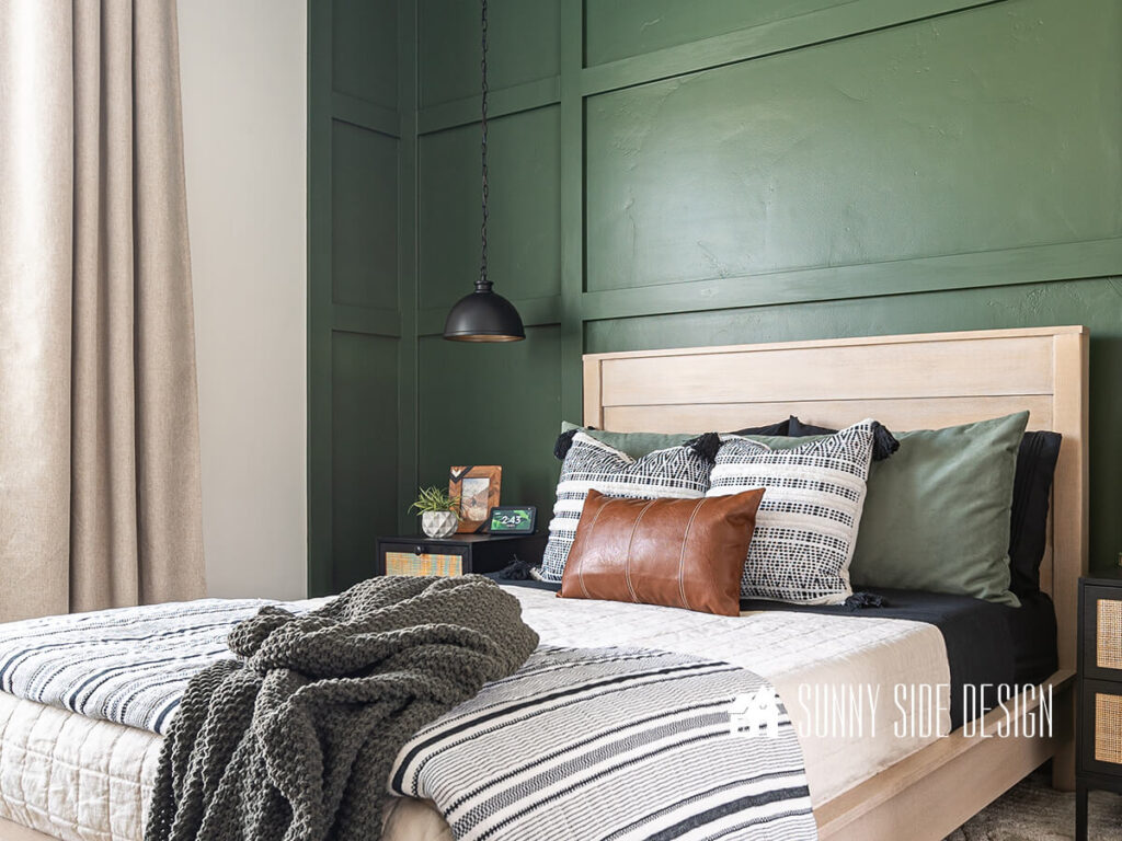 Bedroom home tour, green board and batten wall that extends to the side walls, white oak bed frame with white, black and green bedding. Black pendant lights are hung from the ceiling over the black and rattan nightstands.