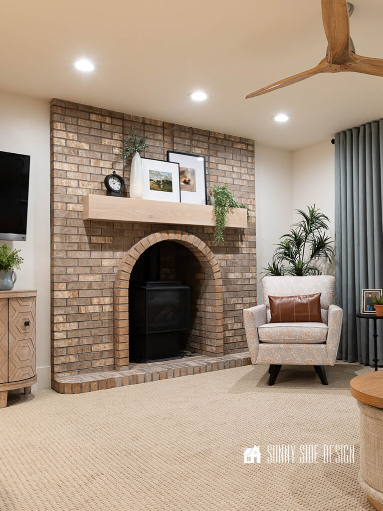 Lighten up a dark room with colorful artwork. Art is matted in white with a modern black frame, placed on the mantle with green plants and a black clock. Swivel side chair with a leather lumbar pillow with a green plant in the background.