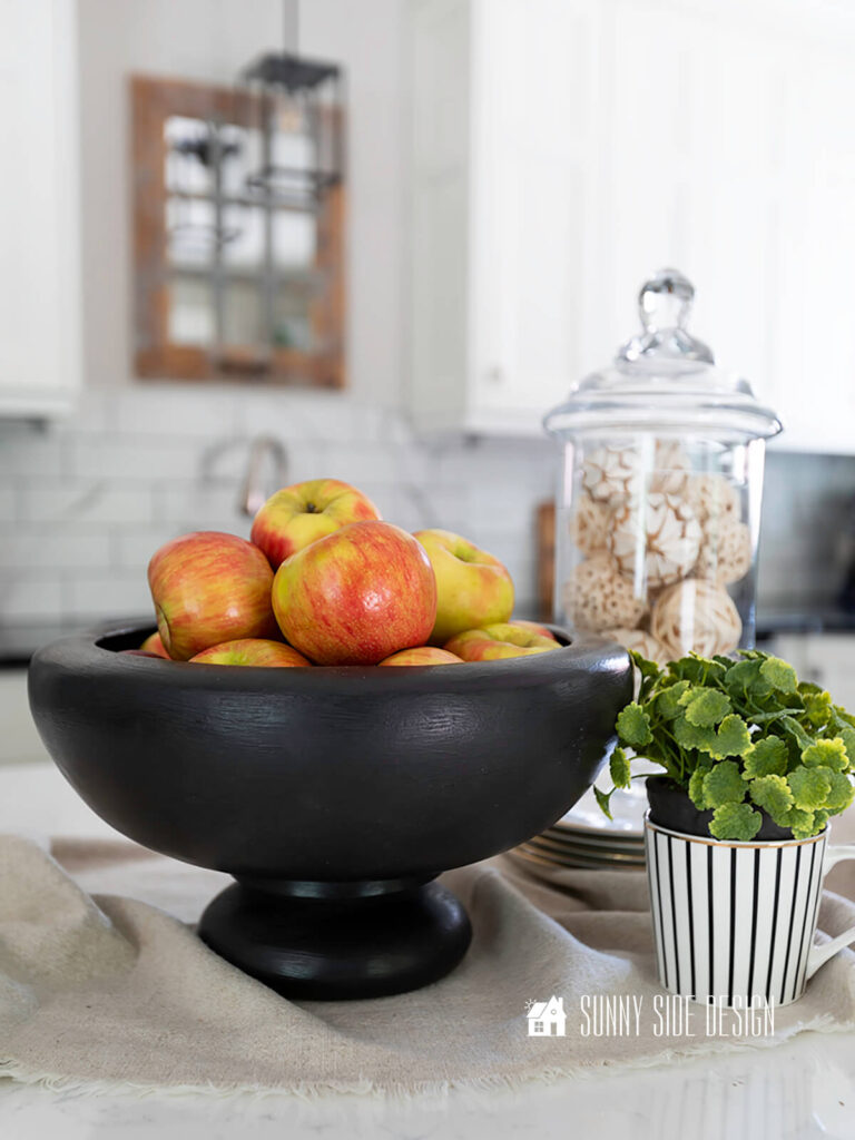 Two thrifted wood bowls are used to create a black pedestal bowl, styled with a plant and apothecary jar filled with spheres.