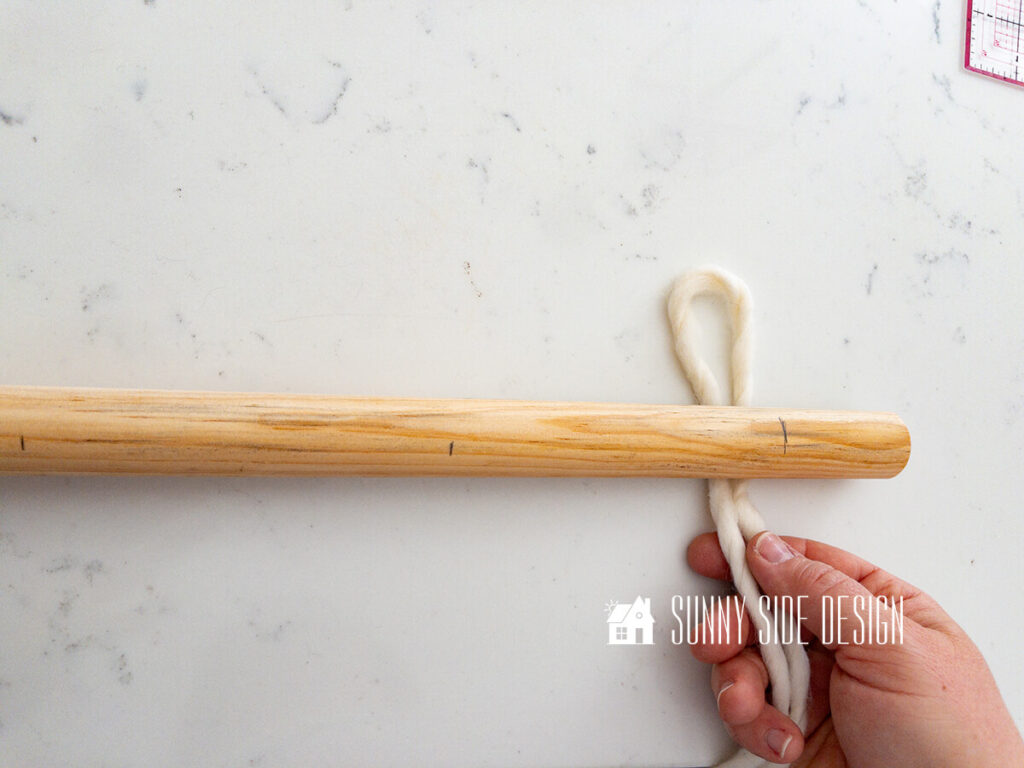 Woman loops cream roving yarn behind the dowel.