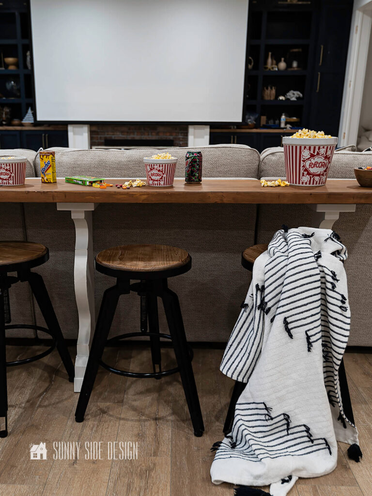 Upcycled Ideas: a wood bench top and tressel kitchen table legs are repurposed into a long sofa table behind a sectional in this theater room.