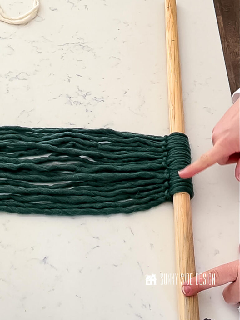 Woman points to placement of the green roving yarn on the dowel for the DIY wall art.