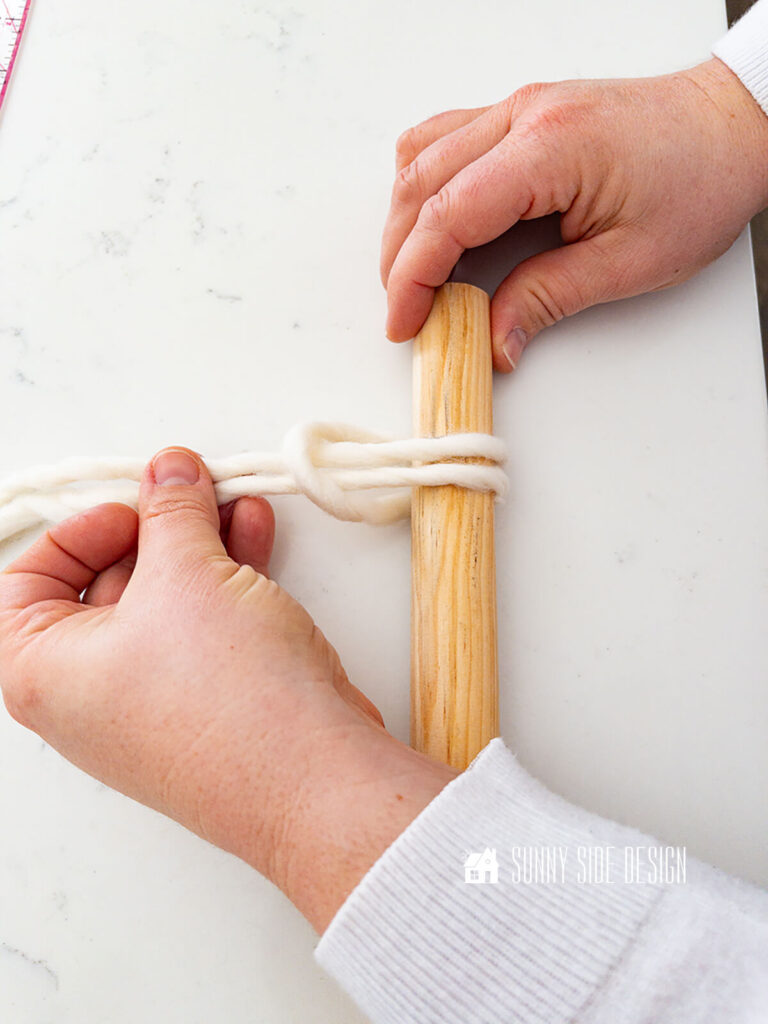 Woman loops doubled yarn around a dowel to form a larks head knot.