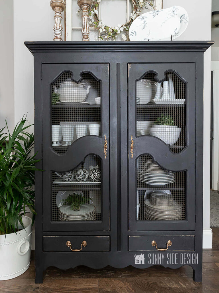 Dated distressed china cabineted is updated with black chalk paint. Styled with white dishes.