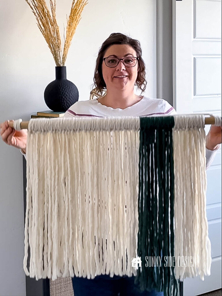 Woman holds completed fiber wall art with cream and green roving yarn.