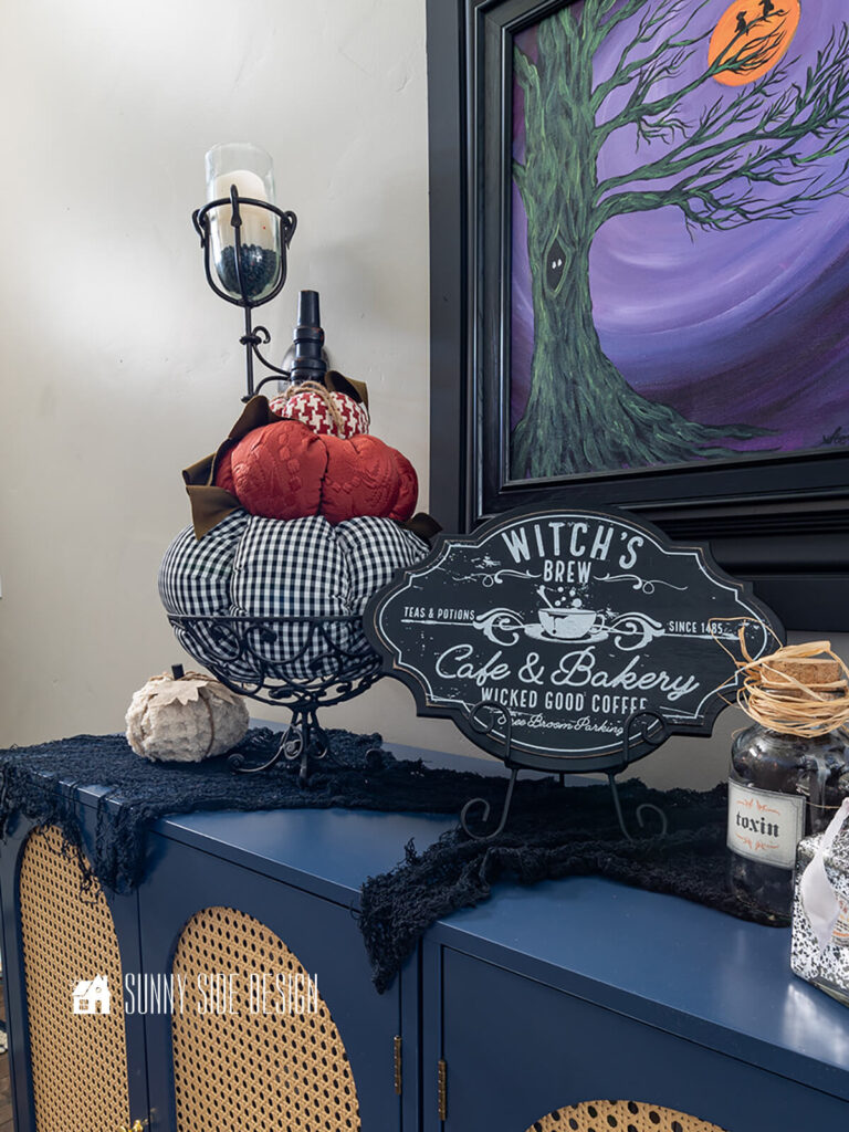 Foyer cabinet Halloween decorating ideas: fabric stacked pumpkin topiary in an iron basket with creepy cloth help add the spooky vibes to the entryway.
