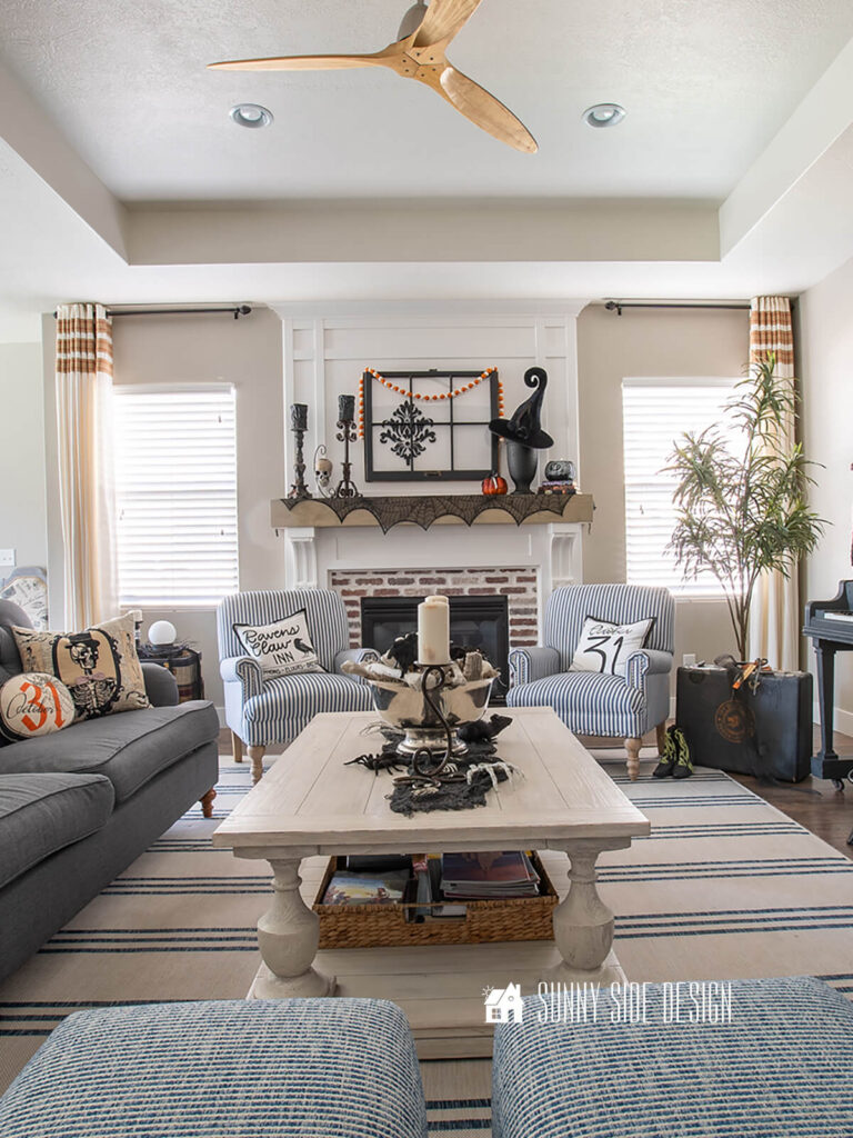 Halloween decorating ideas in the living room: mantle decorated with vintage candlesticks and spooky candles, spider web mantle scarf, hanging skull, velvet witch had pumpkins and witch book stack.