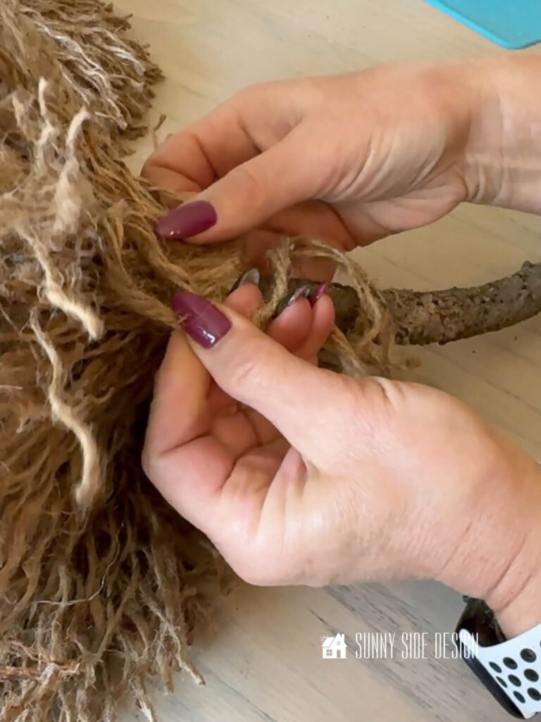 Woman make a loop with jute to finish off the broom.