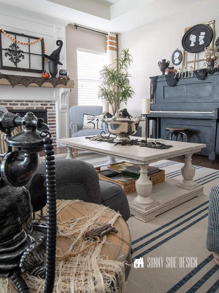 Coffee table decorated for Halloween with a black creepy cloth table runner, thrifted footed silver bowl filled with spanish moss, skeleton bones and black birds.