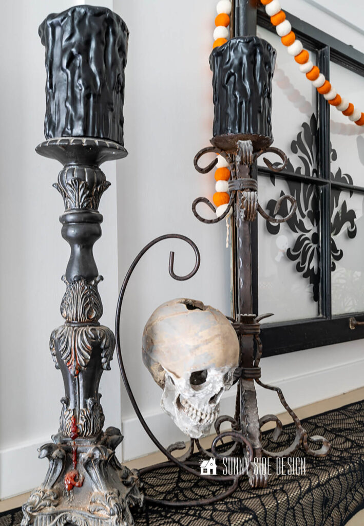 Halloween mantle decorated with vintage candlesticks, spooky black candles and a skull hung from an iron stand.