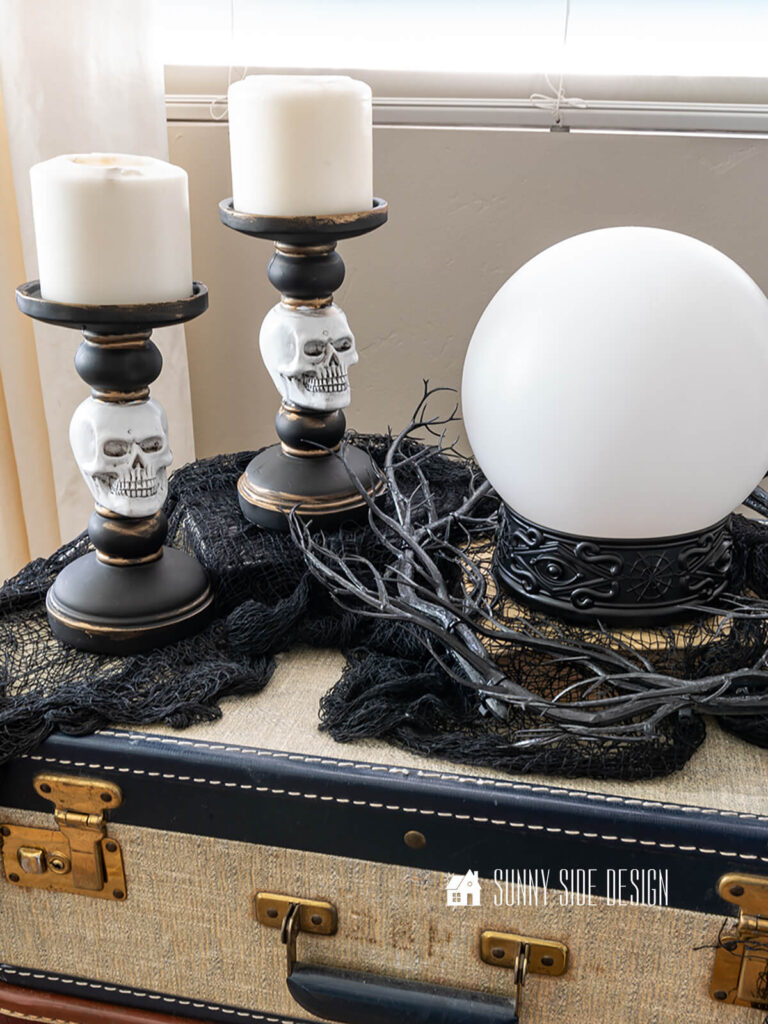 Stacked vintage suitcases in the living room are decorated for Halloween with black creepy cloth, skull candlesticks, spooky twig wreath and a crystal ball.