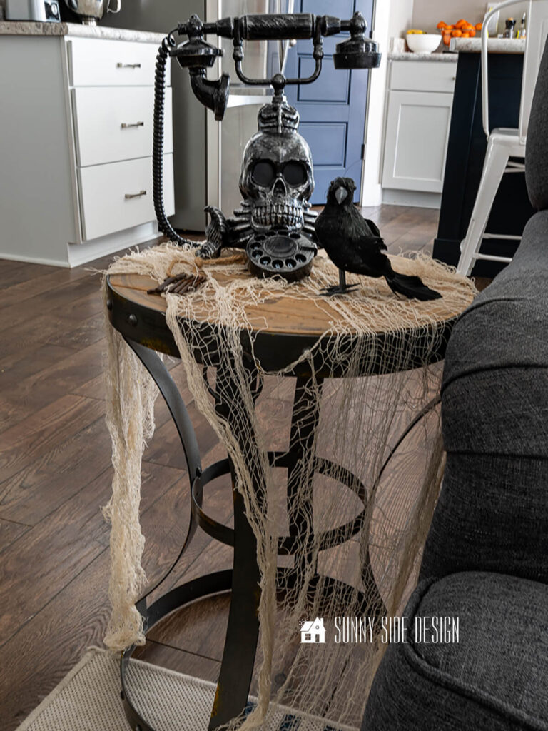 Accent table in the living room is decorated for Halloween draped with white creepy cloth, a skeleton telephone, black bird and vintage keys.