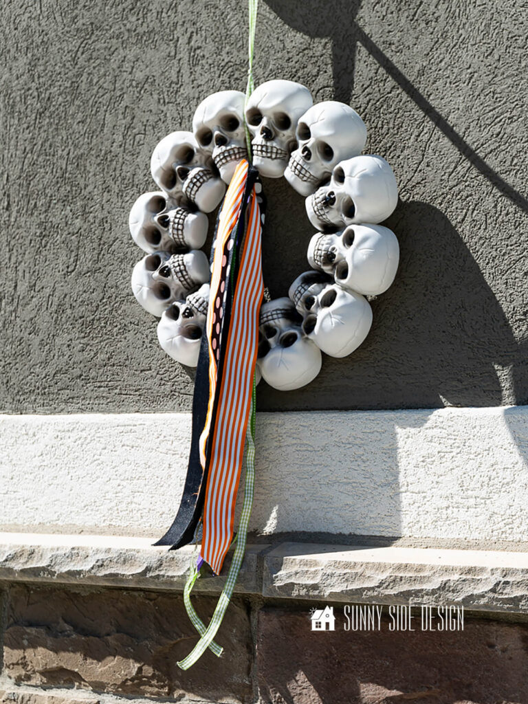 Halloween decorating ideas for outdoor garage lights: Simple $3 skull wreaths are hung on lights and embellished with Halloween colored ribbon.