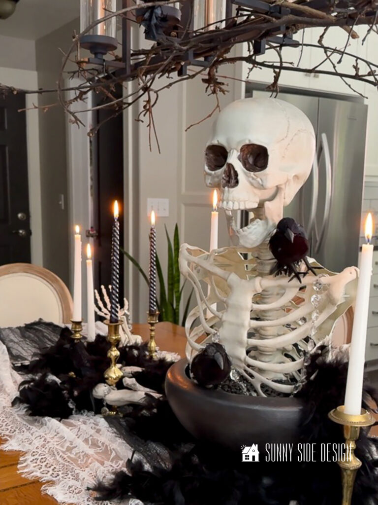 Halloween centerpiece, a skeleton torso and head are placed in a black pedestal bowl and embellished with black birds and vintage chandelier crystals.