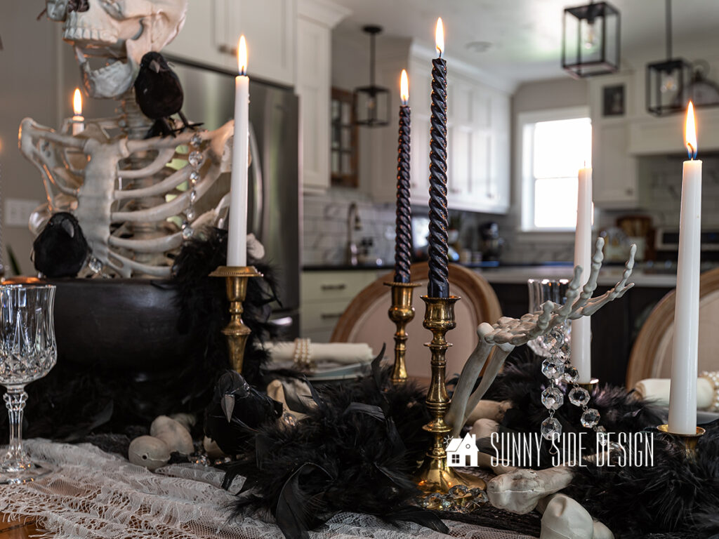 Simple spooky and elegant black and white Halloween tablescape with a skeleton centerpiece, vintage brass candlesticks, lace and creepy cloth tablescape, black birds and feathers and bones scattered down the center of the table.