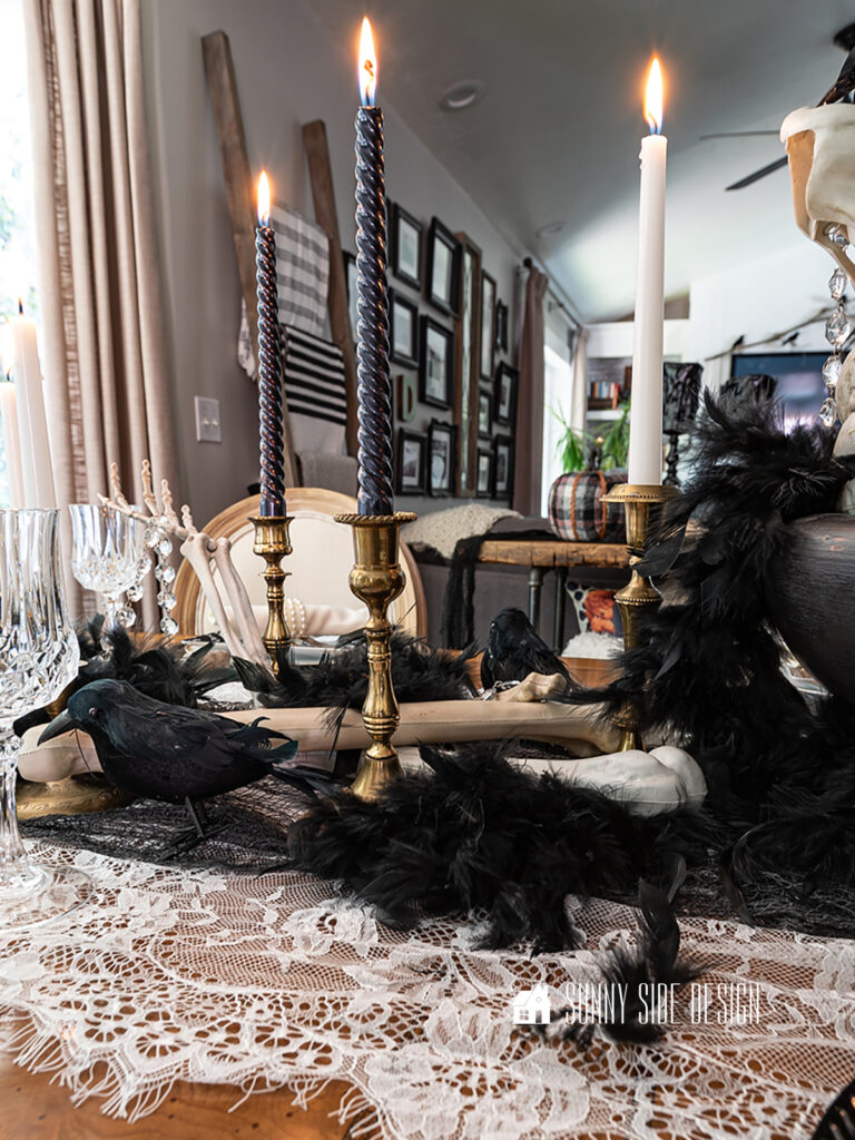 Halloween table decor ideas: skeleton bones are scattered on top of the lace and creepy cloth table runner along with black birds and feathers.