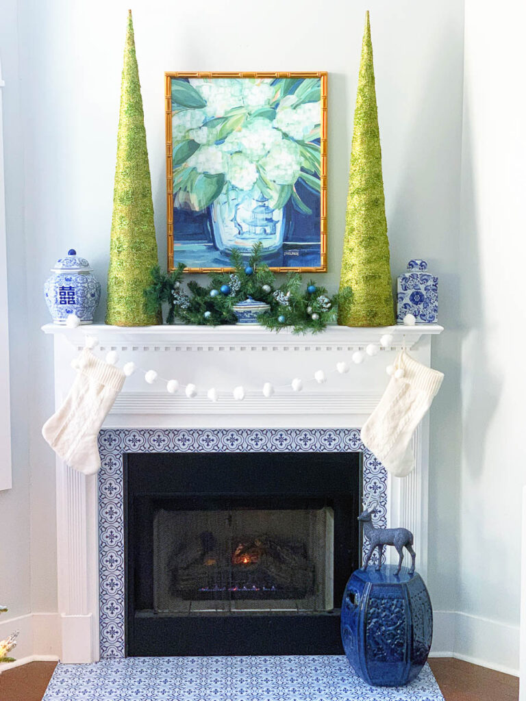 Blue and green Christmas Decorating Ideas for Mantle, two tall green trees, blue and white chinoiserie vases and pine stems with blue ornaments.