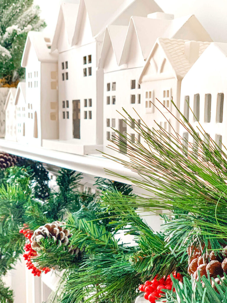 Christmas Decorating Ideas for Mantle with a white Christmas village, along with Christmas garland and trees.