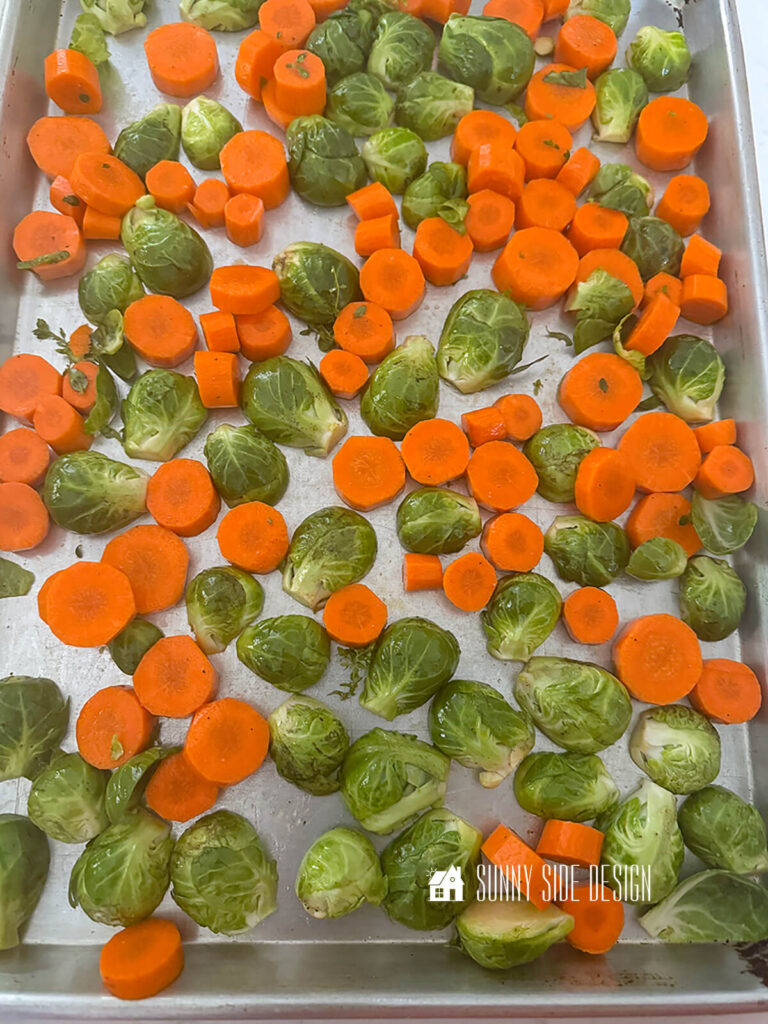 Seasoned halved and sliced carrots spread out on a sheet pan.