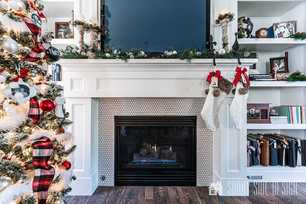 Simple green pine stems and mercury glass ornaments are placed on the mantle with candle sticks flanking the TV.