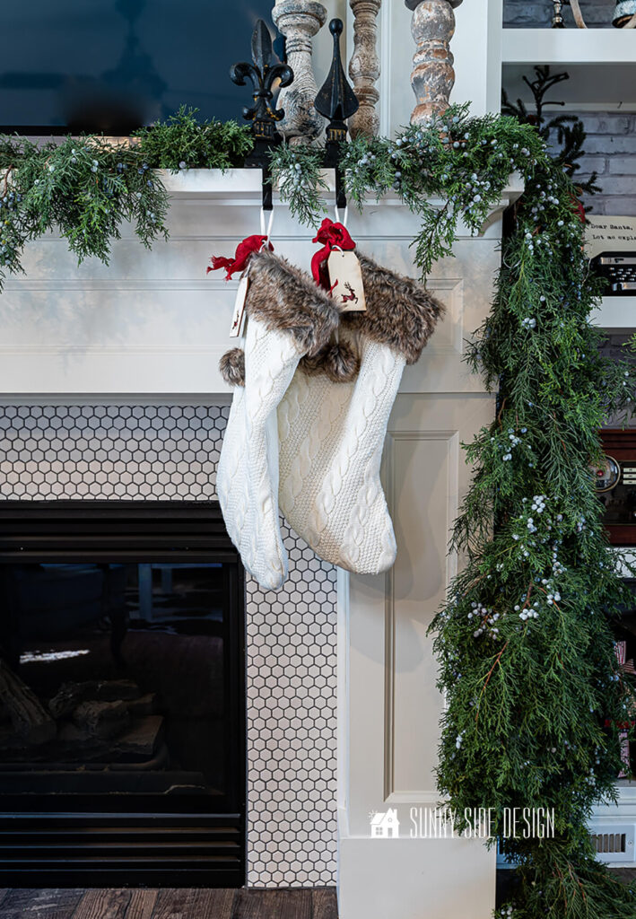 DIy fresh juniper garland is draped over the mantle along with two ivory knit stocking.