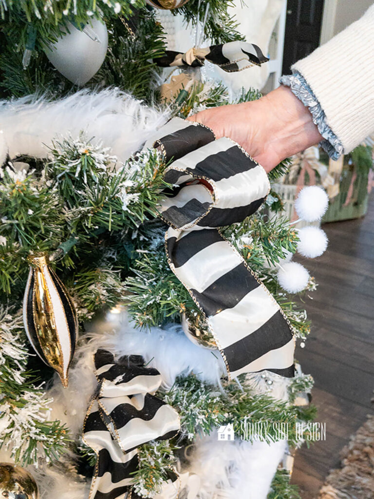 Woman tucks a double looped ribbon into a flocked Christmas tree.