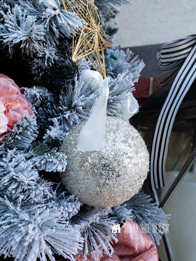 Ivory chiffon ribbon is tied to the tree branch, securing the large ornament to the tree.