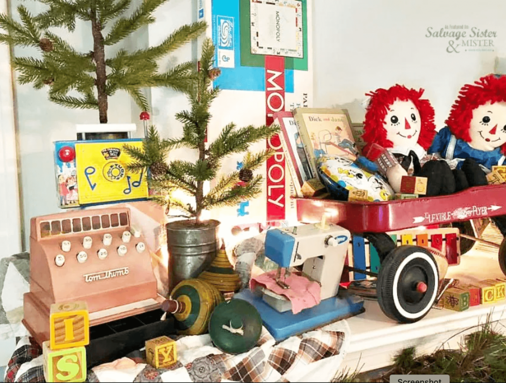 Christmas Decorating Ideas for Mantle with a variety of vintage children's toys including Raggety Ann and Andy, red wagon, monopoly, cash register, sewing machine, blocks, tops and a couple of small potted Christmas trees.