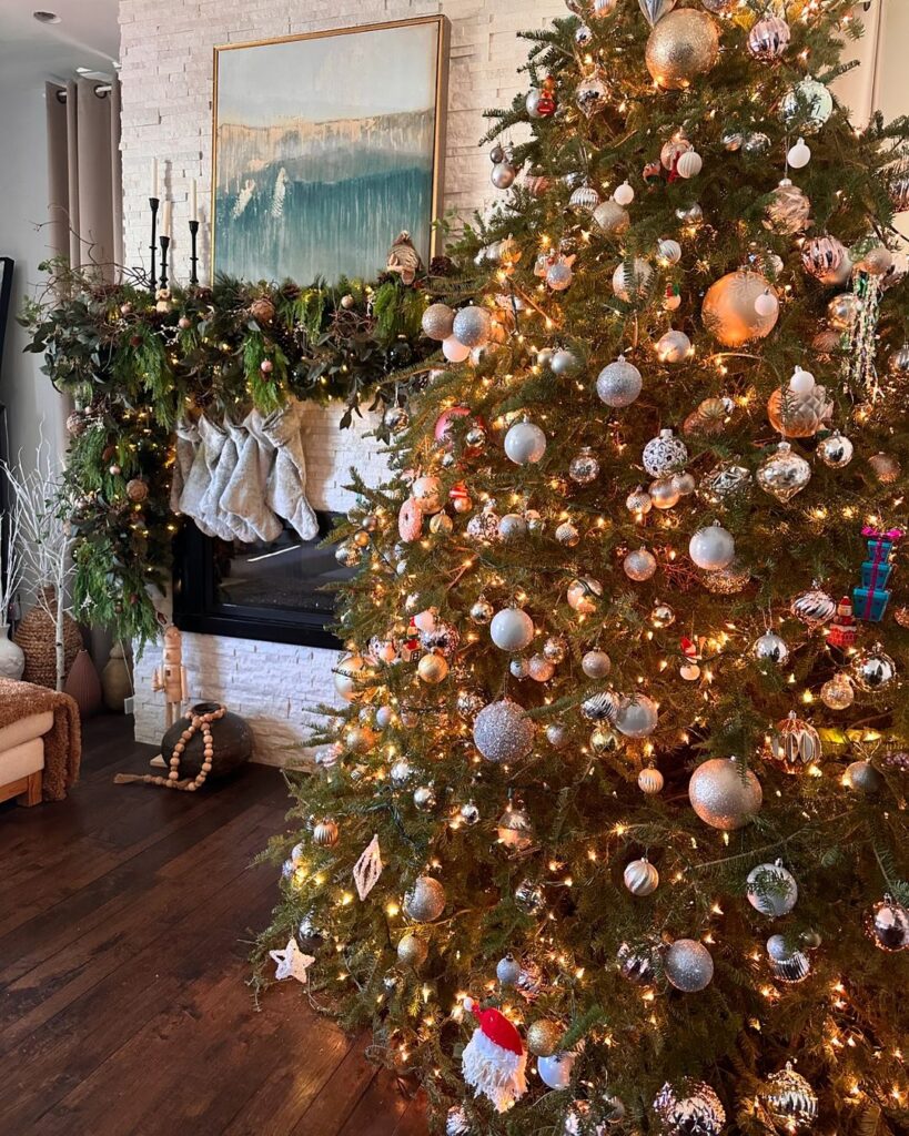 Regency-core Christmas mantle with a extravagant garland draped across the mantle, lights and ornaments. A beautiful Crhistmas tree is in the foreground with a variety of ball ornaments.
