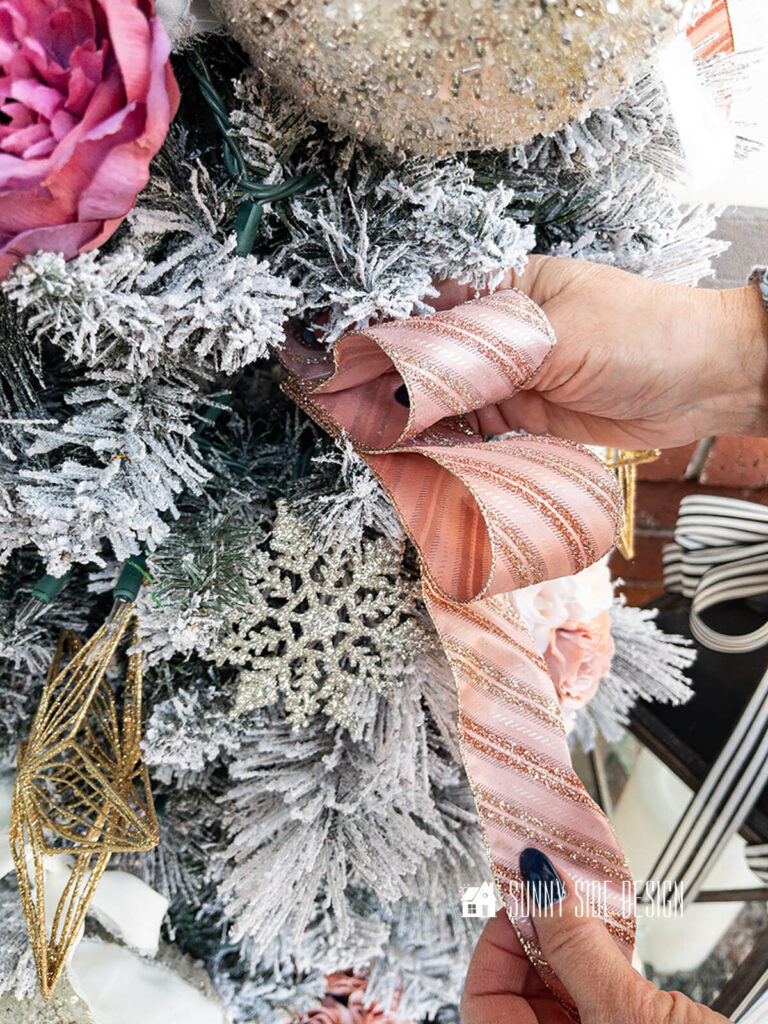 Woman places blush double loop ribbon on a Christmas tree.