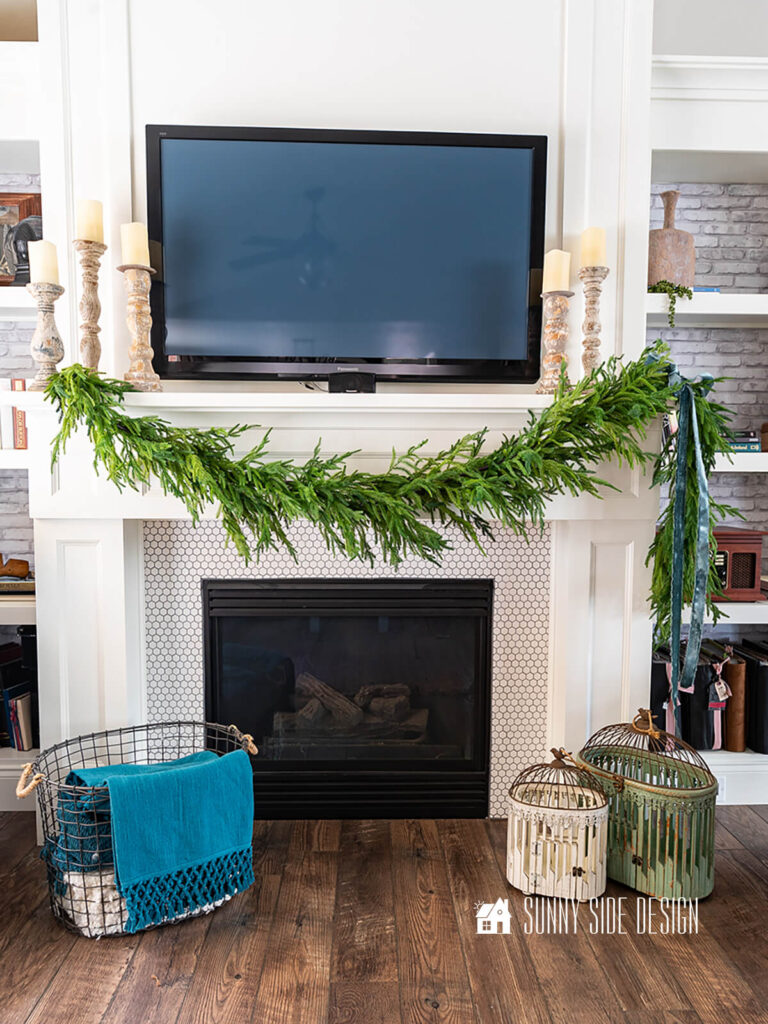 Styled faux pine garland is draped across mantle with a blue velvet box on one side.