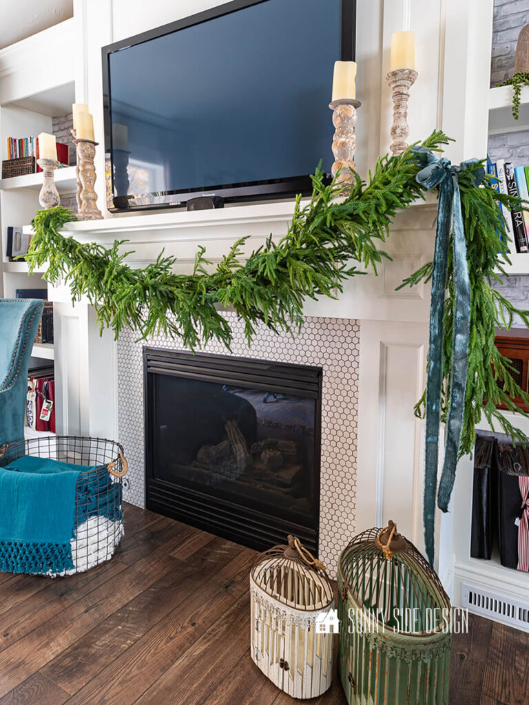 Styled faux pine garland is draped across mantle with a blue velvet box on one side.